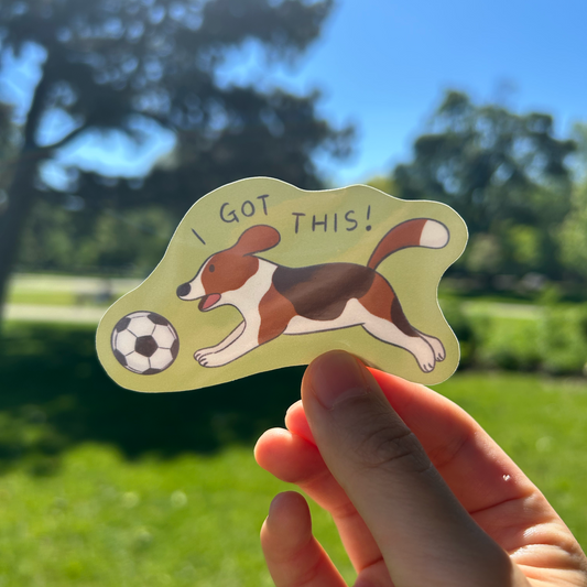 Hand holding a sticker with a dog and soccer ball design outdoors.