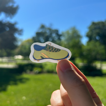 Hand holding a sticker with a blue and yellow design against a blurred outdoor background