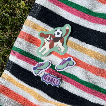 Colorful striped towel with a dog playing soccer sticker and small stickers of soccer cleats and "goal!" sticker
