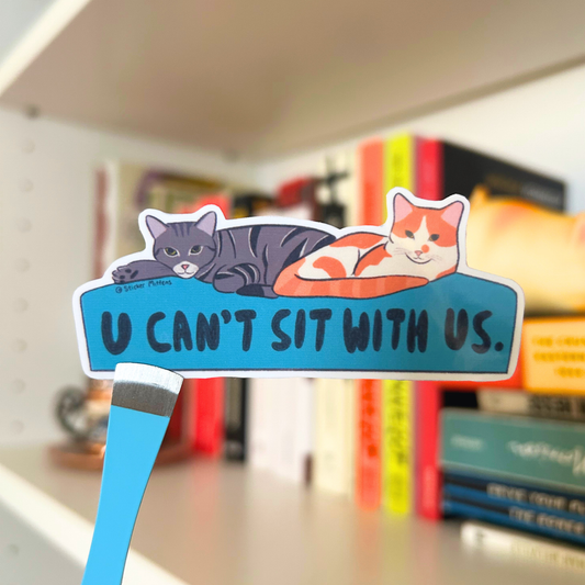 Sticker with two cats lounging on a bed with text 'U CAN'T SIT WITH US' 
