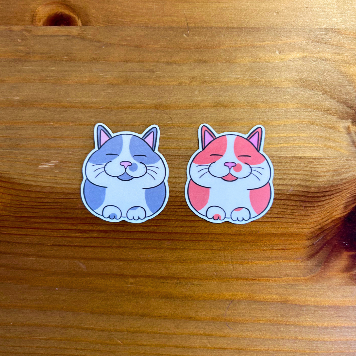 Two cartoon cat stickers on a wooden surface
